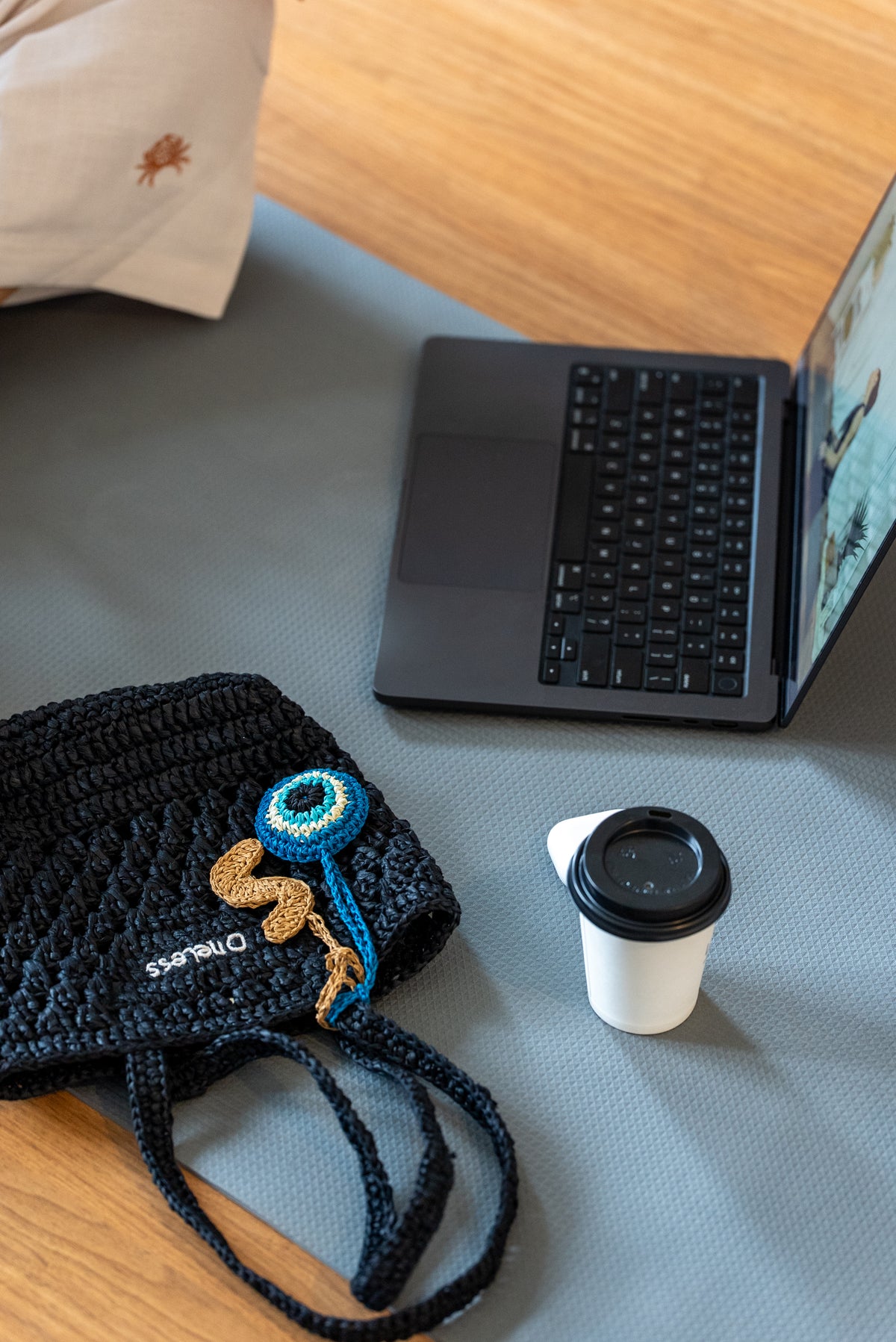 Black raffia bag with crochet evil eye charm styled next to a laptop and coffee cup
